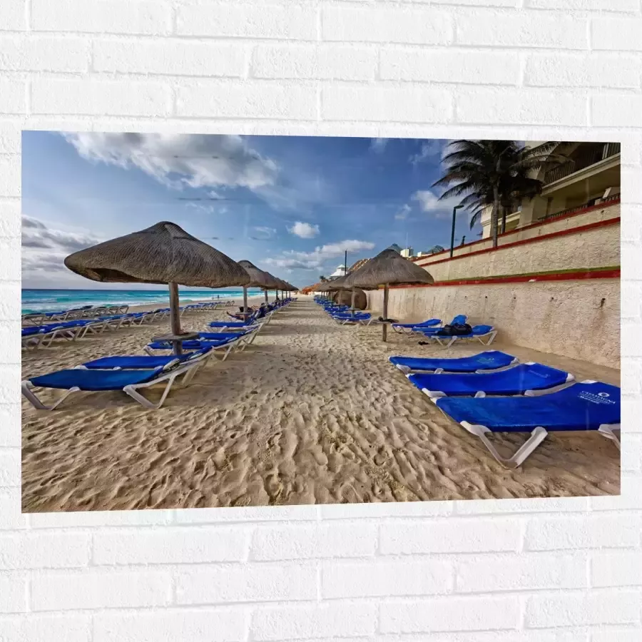 WallClassics Muursticker Blauwe Ligbedden op Strand met Rieten Parasols 105x70 cm Foto op Muursticker