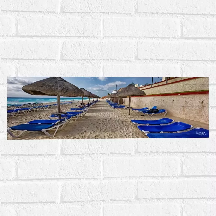 WallClassics Muursticker Blauwe Ligbedden op Strand met Rieten Parasols 60x20 cm Foto op Muursticker