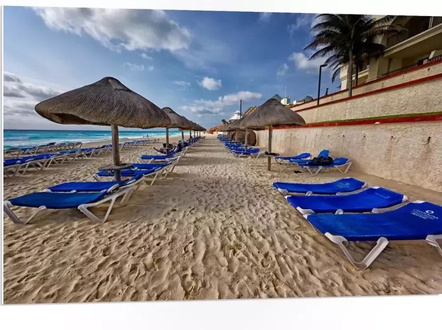 WallClassics PVC Schuimplaat- Blauwe Ligbedden op Strand met Rieten Parasols 105x70 cm Foto op PVC Schuimplaat