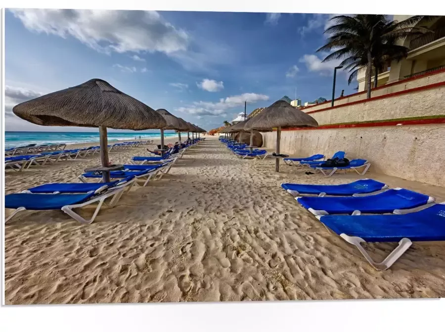 WallClassics PVC Schuimplaat- Blauwe Ligbedden op Strand met Rieten Parasols 75x50 cm Foto op PVC Schuimplaat