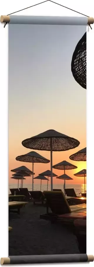WallClassics Textielposter Ligbedden met Rieten Parasols aan het Strand in de Avondzon 30x90 cm Foto op Textiel
